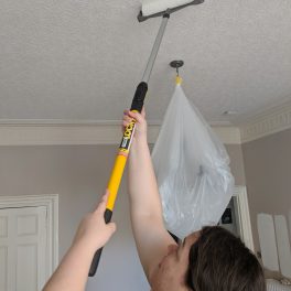 Alex using a long roller to paint the ceiling