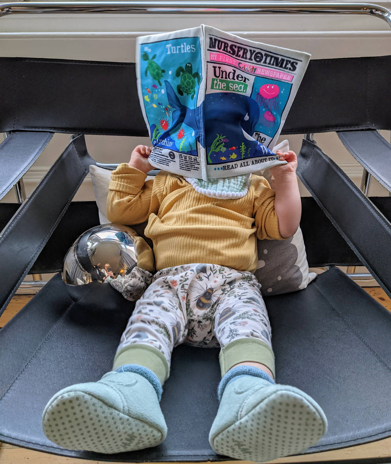 Izzy with her face obscured by her baby sensory newspaper