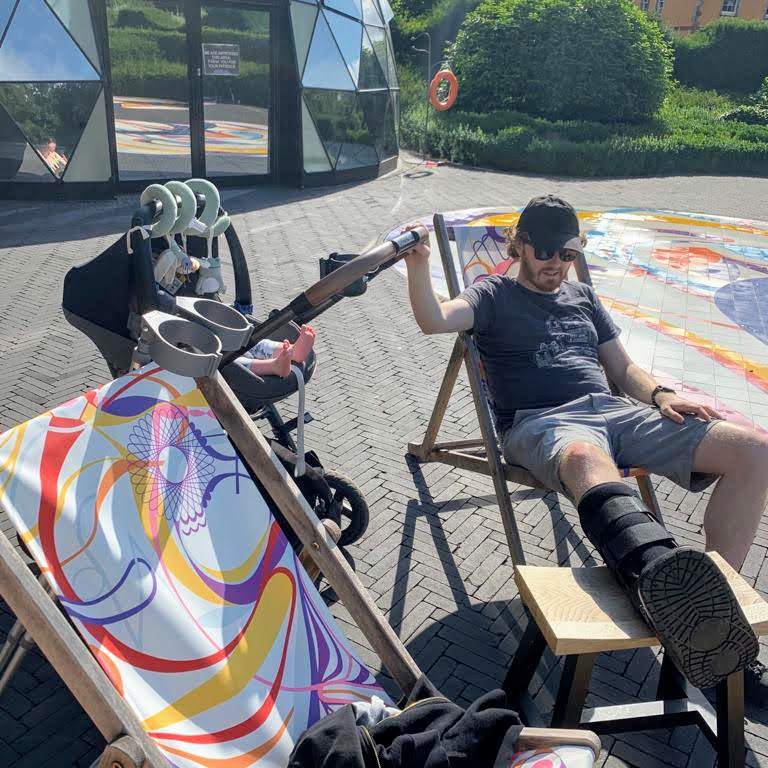 Me, with my leg elevated, in a moon boot; I'm rocking Izzy to sleep in her buggy while we sit in the sun next to a swimming pool