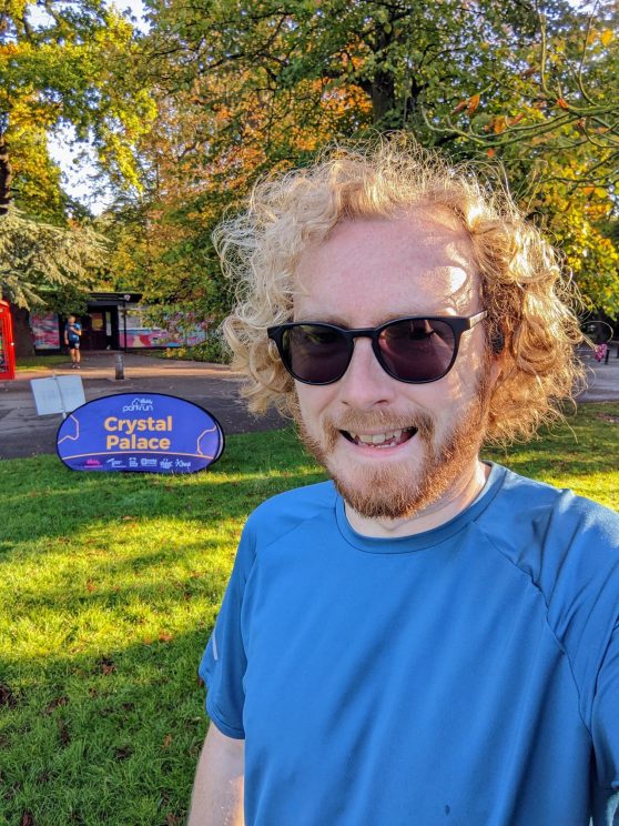 Me wearing sunglasses next to the Crystal Palace parkrun sign